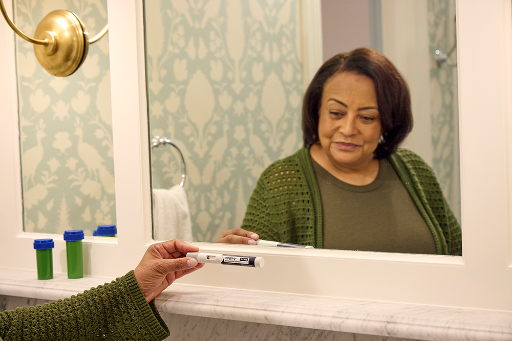 An older woman staring at her Wegovy injectable pen in a bathroom.