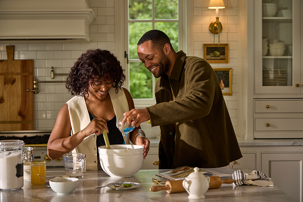 A young couple mixing ingredients together in an upscale kitchen.
