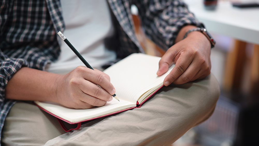 A man writing down his stress triggers in a journal.