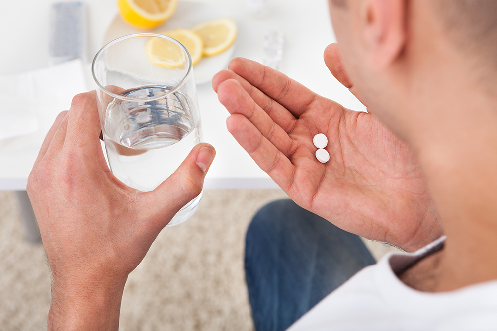 A person holding two pills with a glass of water.