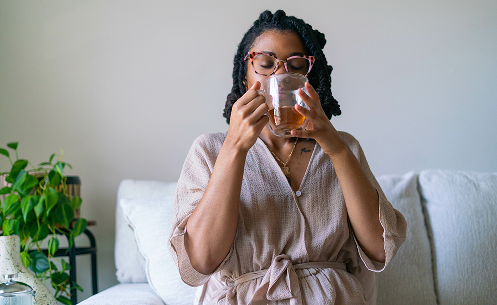 A woman drinking herbal tea on a sofa.