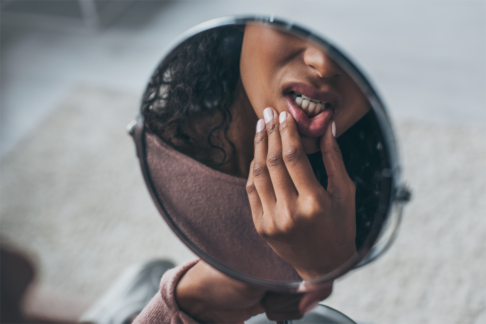 A woman examines her gums in the mirror.