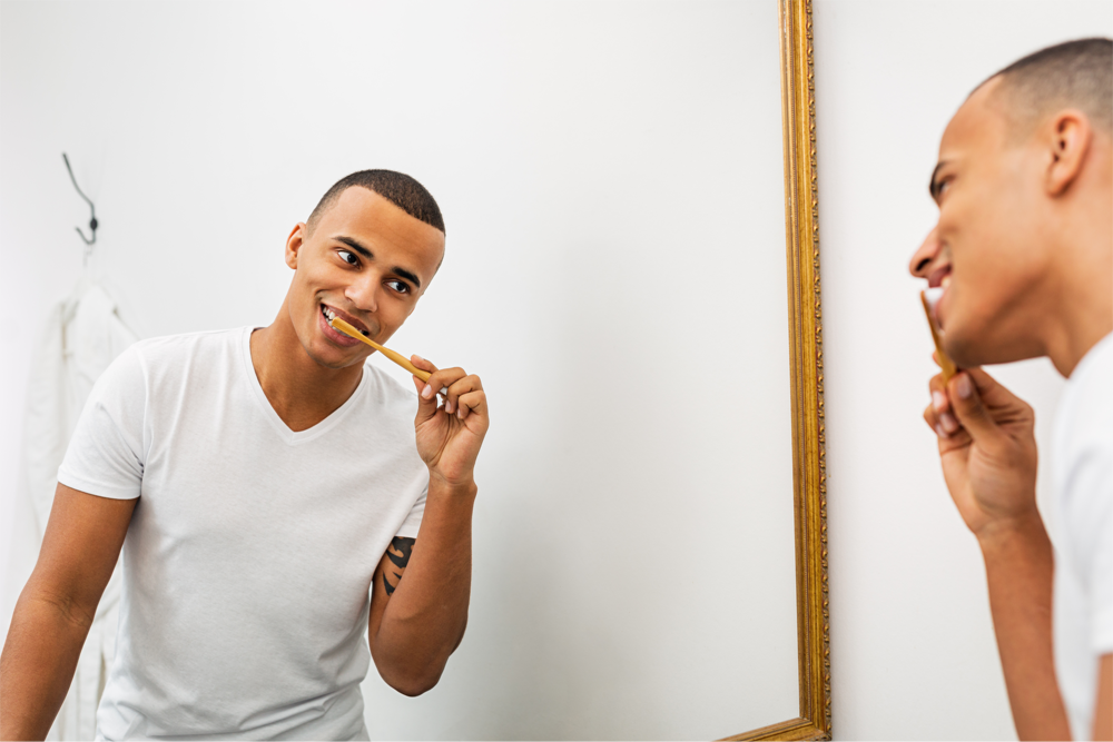 A man brushes his teeth while looking at his reflection.