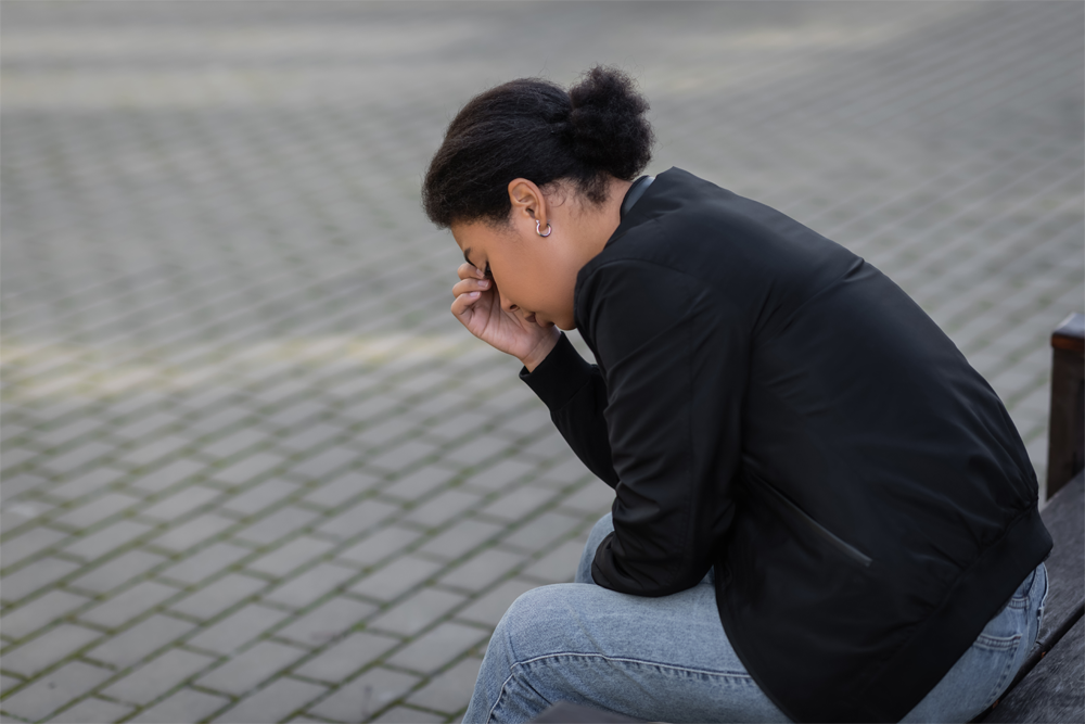 A woman is visibly stressed on an outdoor bench.