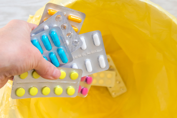 A patient is seen tossing foil packs of medication into a trash can.