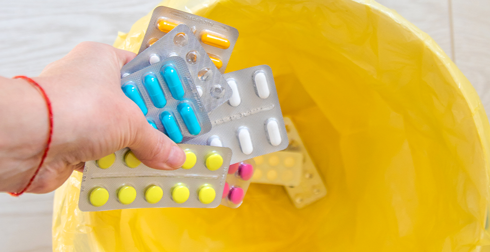 A patient is seen tossing foil packs of medication into a trash can.