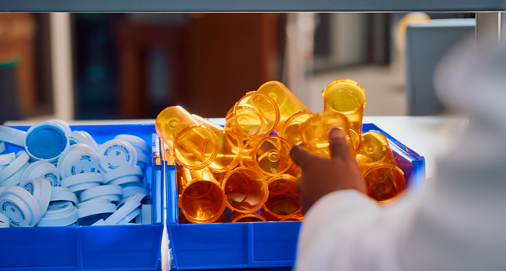 A pharmacist grabs a pill bottle from a bin.