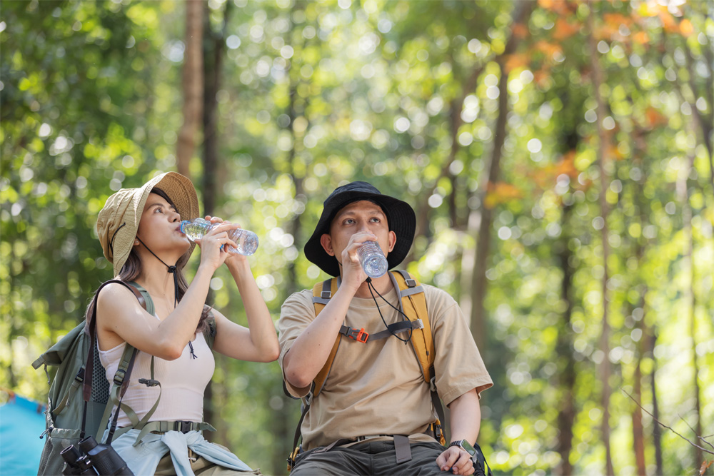 Two travelers sip water while backpacking through a forest.
