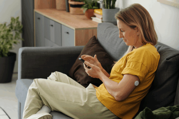 A woman browses her phone wearing a CGM on her arm.