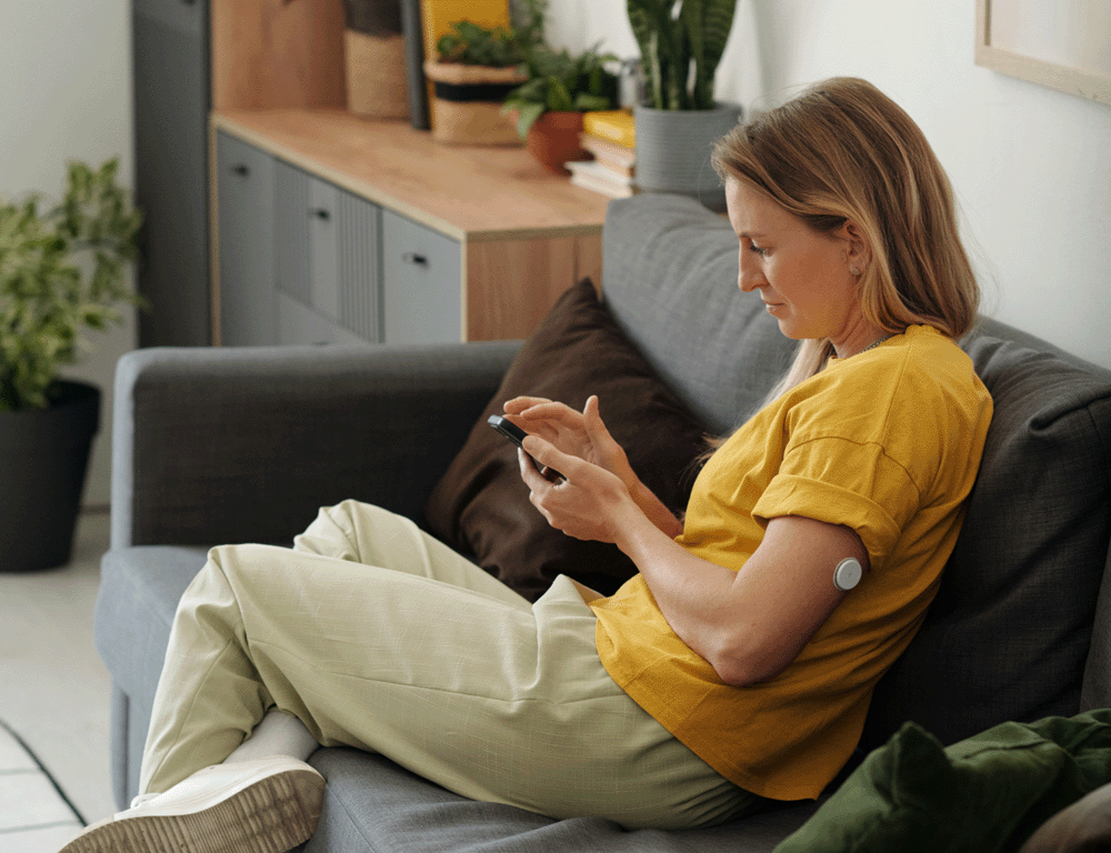 A woman browses her phone wearing a CGM on her arm.