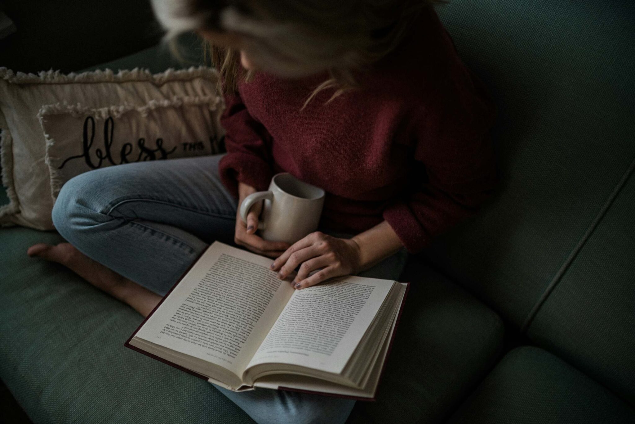 Woman reading as she soothes her perimenopause symptoms with warm tea.