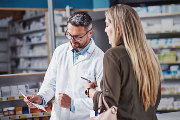 A pharmacist reviewing a prescription for a customer at a drugstore counter.