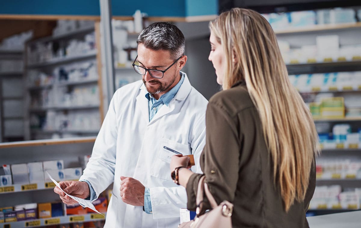 A pharmacist reviewing a prescription for a customer at a drugstore counter.