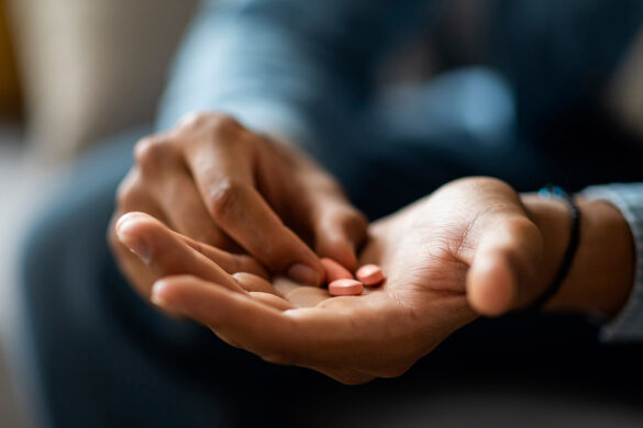 A close-up view of a person pouring pills from an orange bottle into their open palm.
