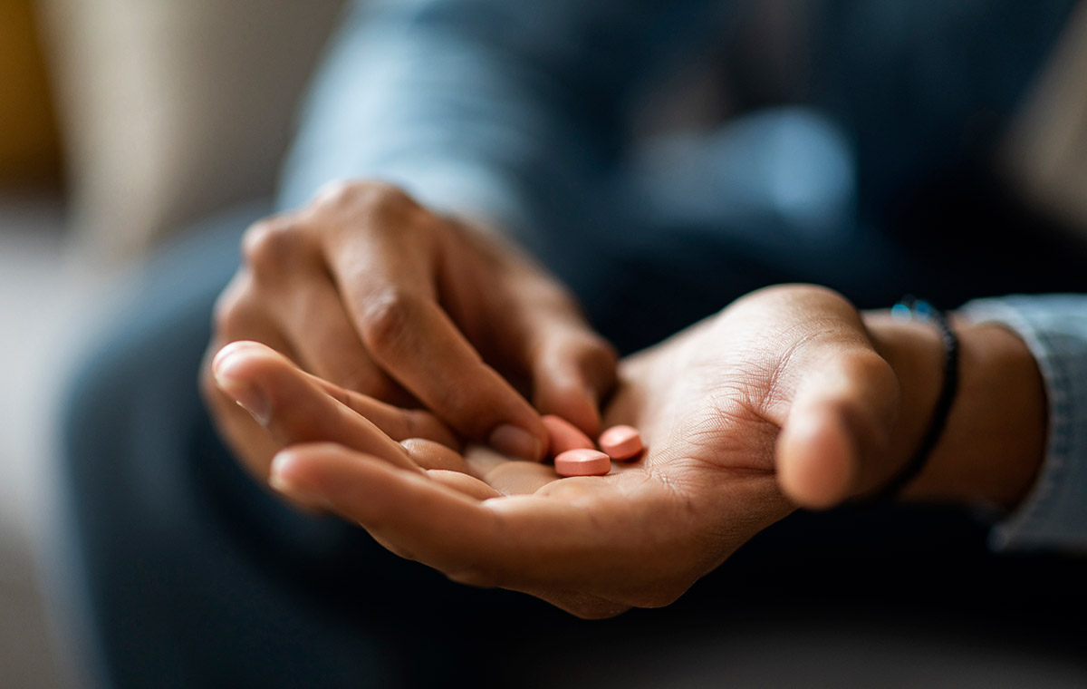 A close-up view of a person pouring pills from an orange bottle into their open palm.